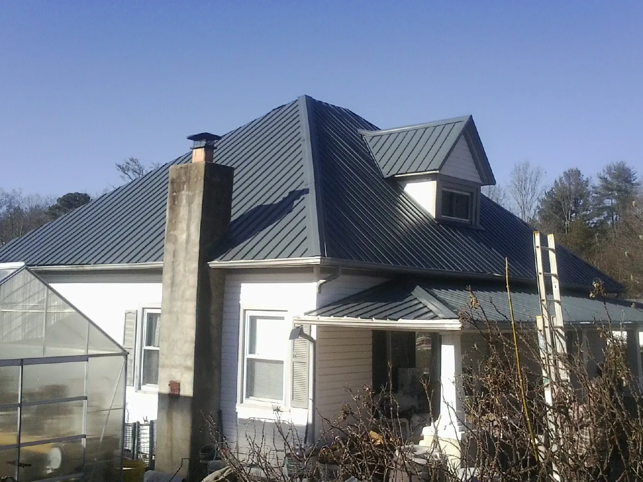 Dark blue standing seam metal roof on a white farmhouse with dormer — Slate & Tile Roof Repair by Roofing Brothers in Chesterville