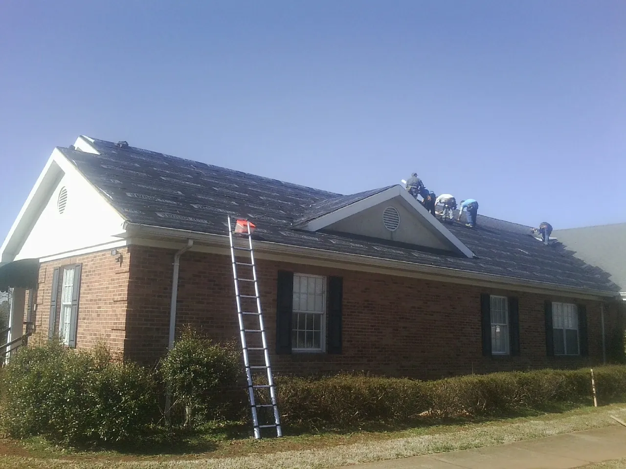 Crew tearing shingles off a brick ranch roof with a ladder set — Emergency Roof Repair work by our crew in Chesterville