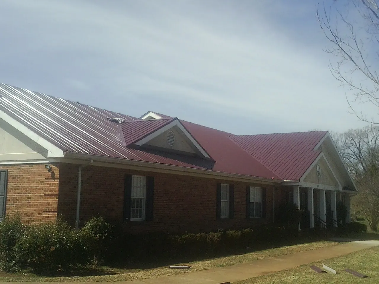 Red metal roof with gabled entries on a long brick building, from a Hail Damage Roof Repair job in Chesterville