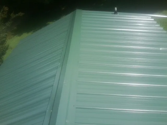 New green metal panels meeting at the ridge of a roof — Flat Roof Repair work by our crew in Chesterville