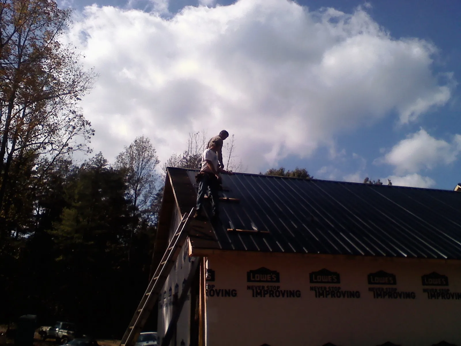 Roofer fastening dark metal panels high against a cloudy sky, from a Roof Inspection job in Chesterville