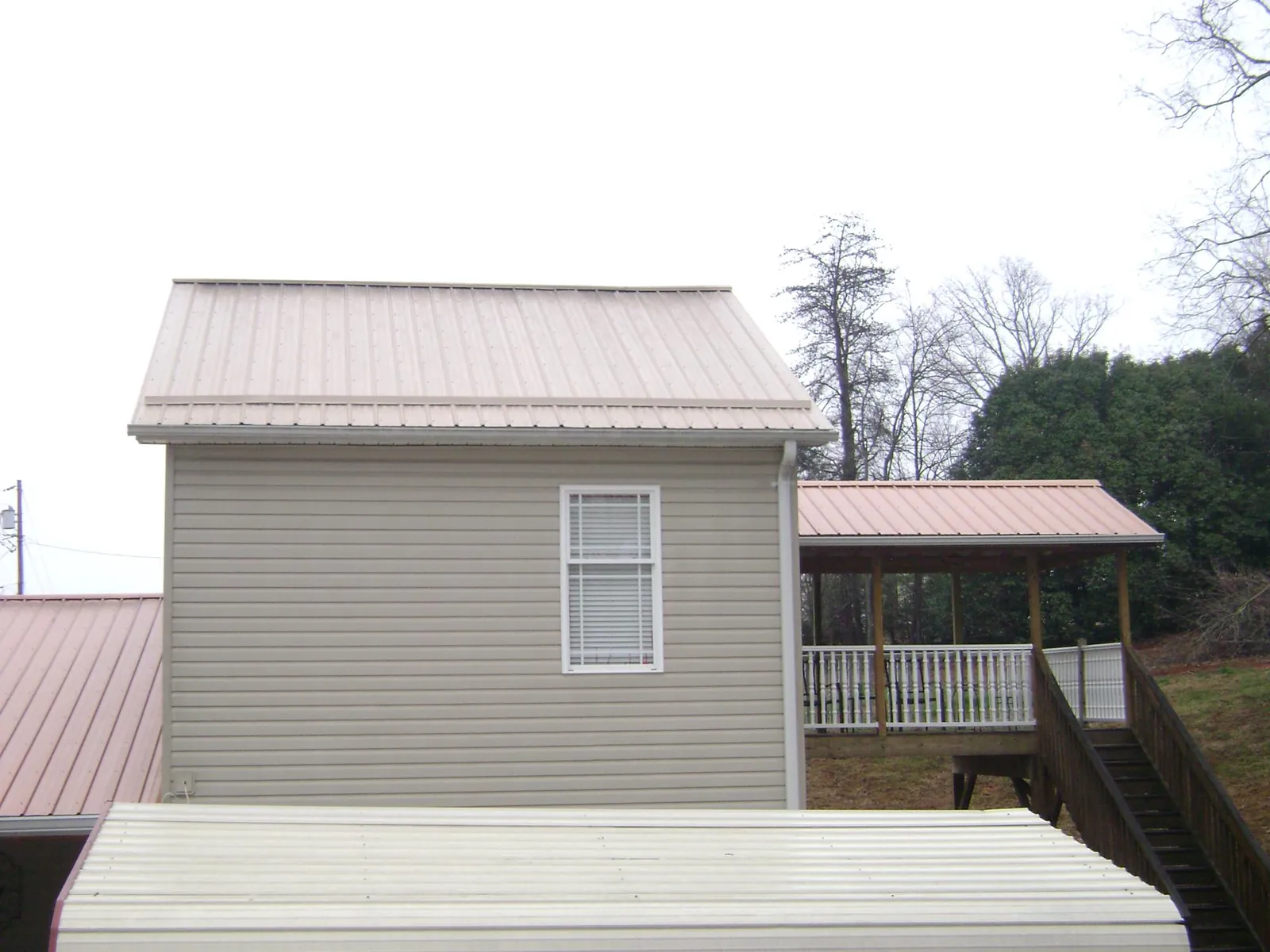 Tan metal roofs on a two story addition and attached porch, from a Roof Replacement job in Chesterville